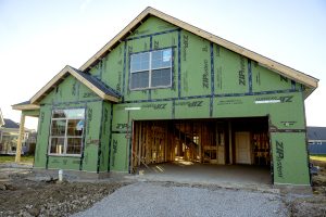 gravel driveway leading up to green sided exterior of home in the process of being built